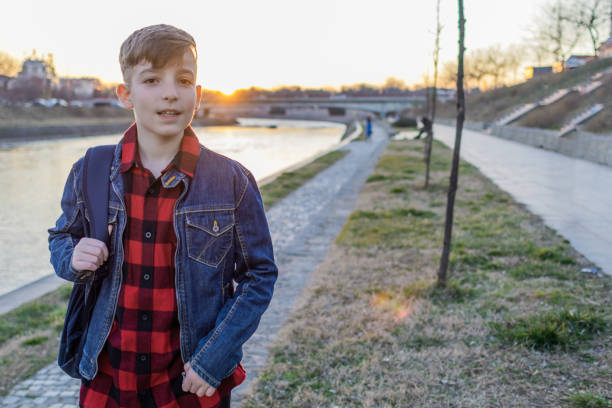 Cute boy is walking near the river at sunset.