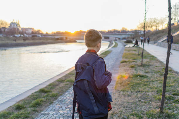 Cute boy is walking near the river at sunset.