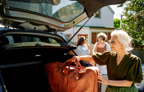 femme mûre emballant des bagages dans une voiture pour un voyage en voiture avec des amis - active seniors enjoyment driveway vitality photos et images de collection