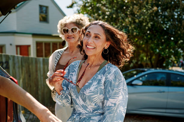 mature female friends smiling while leaving for a road trip together - active seniors enjoyment driveway vitality imagens e fotografias de stock