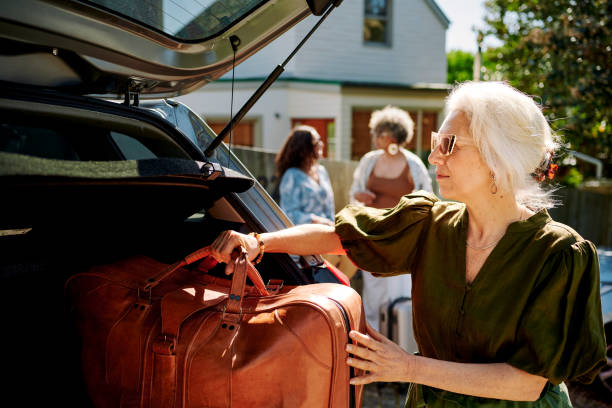 femme mûre emballant des sacs dans une voiture pour un voyage en voiture avec des amis - active seniors enjoyment driveway vitality photos et images de collection