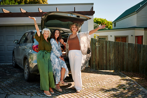 Portrait of a group of ecstatic mature female friends standing at the trunk of their car full of luggage in a driveway before leaving for a weekend getaway together
