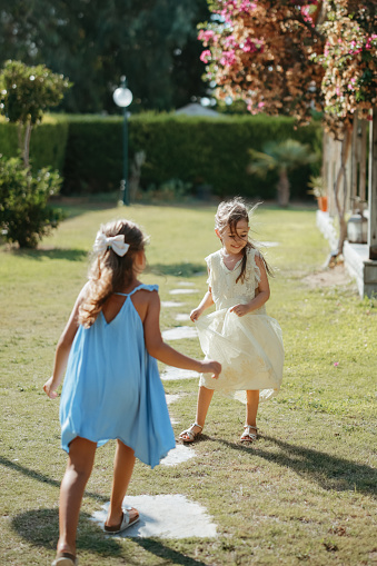 Sisters in similar outfits holding hands and running on grass while playing in summer park together