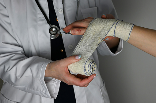 a doctor in a white coat with a stethoscope bandages the hand of an adult woman.