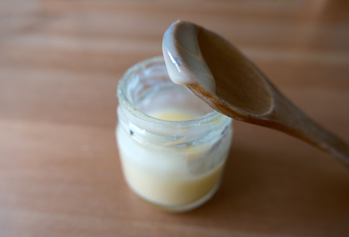 Royal jelly in a little jar. It's also called bee milk. Focused on the drop in wooden spoon.
