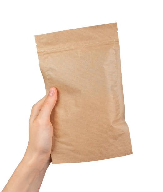 A hand holding a brown paper bag A hand holding a brown paper bag. Ziplock pouch, zip-lock packet isolated on white pouch stock pictures, royalty-free photos & images