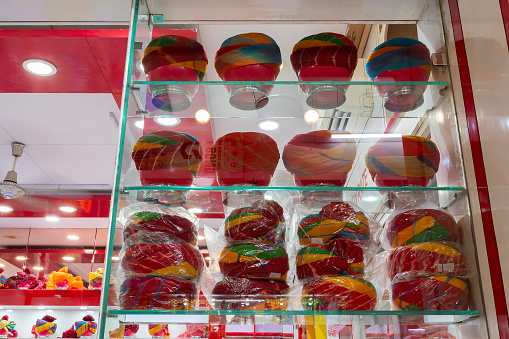 Display of modern turbans, headwear based on cloth winding with many variations, customary headwear for many. Bright, colorful men's costume displayed under glass show case. Jodhpur, Rajasthan, India.