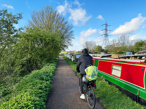 Cyclist by canal boats mored along the River Lee Navigation canal in Tottenham, London. March 2024