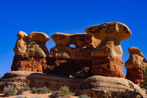 Red Rock Hoodoos Desert Landscape - Scenic views in nature on sunny blue sky day of red rock formations. Rock arch forming in middle area with blue sky showing through.