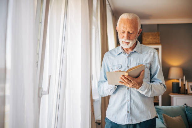 istock Senior man reading book at home 2117765875