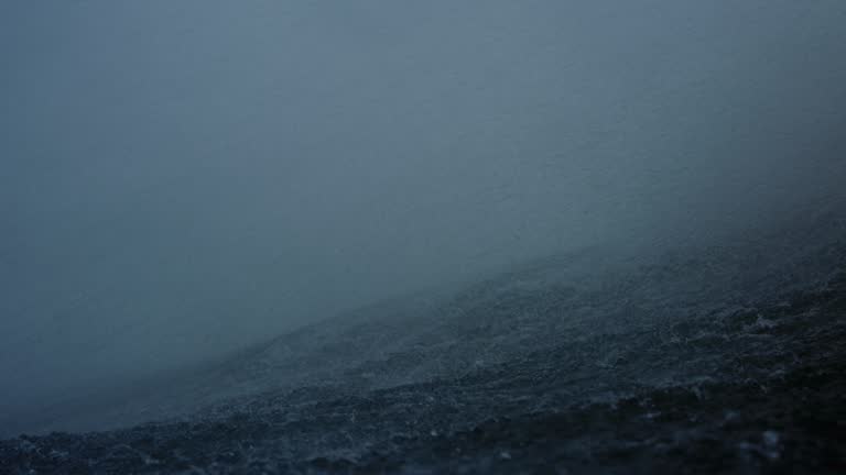 Ocean water spray and mist blows over top of wave on stormy day, slow motion in water