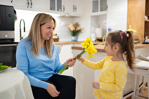 Caucasian girl giving daffodils flowers to her mother, for an International women's day