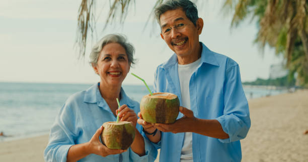 istock Asian elderly cheerful couple smile looking at camera and drinking coconut on beach enjoying the sea view. A happy senior adult people enjoy the travel lifestyle after retirement. 2117809050