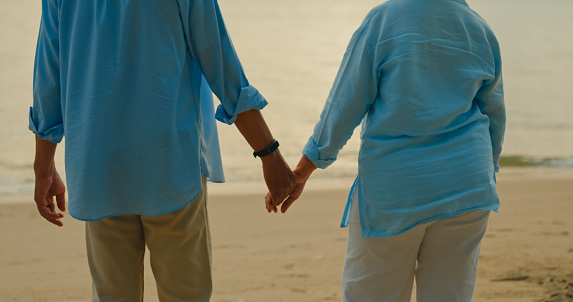 Closeup of Asian elderly cheerful couple holding each other hand on beach enjoying the sea view. A happy senior adult people enjoy the travel lifestyle after retirement concept.