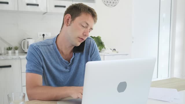 Serious businessman trader talking on phone call while work on laptop at home. Male professional broker investor working online on stock market