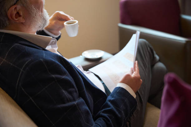 istock Obscure face of businessman with papers drinking coffee from cup on sofa 2117887789