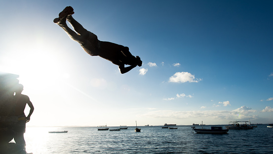 Salvador, Bahia, Brazil - May 31, 2019: Young native, in silhouette, is seen jumping from the Porto da Barra pier in the city of Salvador, Bahia.