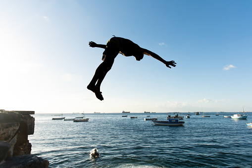 Salvador, Bahia, Brazil - May 31, 2019: Young native, in silhouette, is seen jumping from the Porto da Barra pier in the city of Salvador, Bahia.