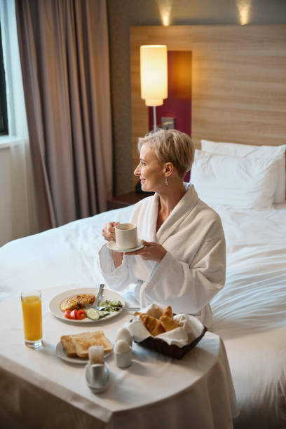 istock Smiling woman looking away and drinking tea or coffee during having breakfast 2117926219
