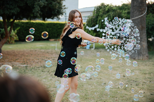 Happy woman entertainer playing with huge bubbles with small kids at birthday party. Smiling female have fun entertain children with game activities.