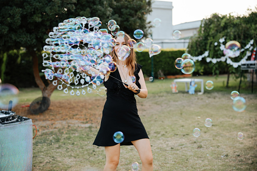 Happy woman entertainer playing with huge bubbles with small kids at birthday party. Smiling female have fun entertain children with game activities.