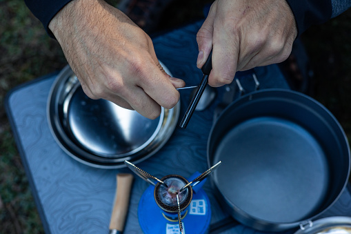 An overhead perspective captures hands igniting a camping stove using a flint, showcasing the traditional method of fire starting in outdoor settings