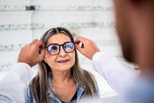 Senior woman trying on glasses and talking with optician at optics