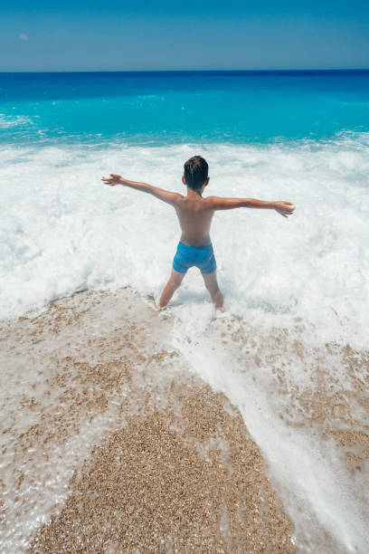 Boy enjoys playing with the waves on his summer vacation on the beautiful Greek Lefkada island