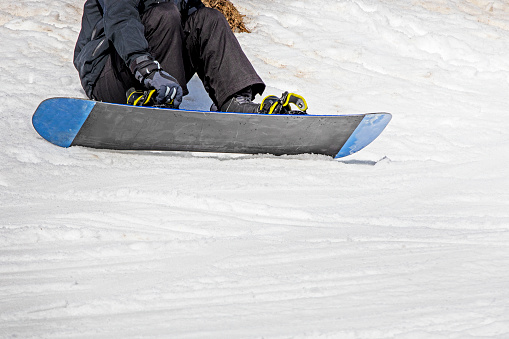 snowboarder sits on a snowboard on wet, loose snow before skiing. active recreation