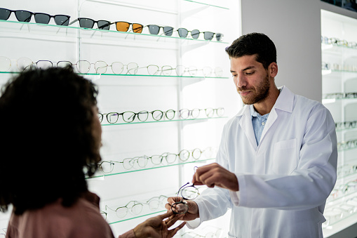 Mid adult optician man selling glasses to customer at the optics