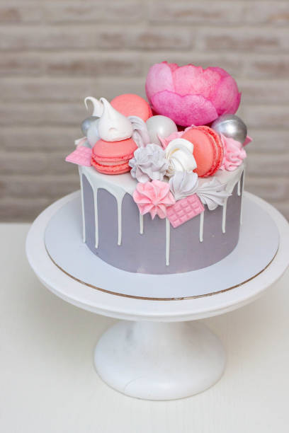 istock Beautiful and elegant grey cake decorated with melted white chocolate, macaroons, pink peony flower and meringues. Idea for wedding or birthday 2118047612