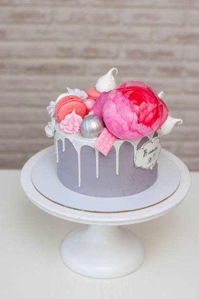istock Beautiful and elegant grey cake decorated with melted white chocolate, macaroons, pink peony flower and meringues. Idea for wedding or birthday 2118047614