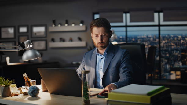 istock Smiling manager answering call at evening office closeup. Calm man talking phone 2118120572