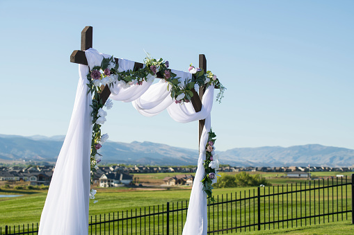 Festive arch decorated with composition of flowers and greenery in the backyard banquet area. Wedding ceremony with decor.