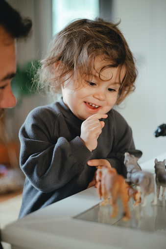Happy father and little daughter playing with toy dinosaurs close up, sitting on warm floor with underfloor heating, smiling dad and overjoyed girl child enjoying leisure time at home together
