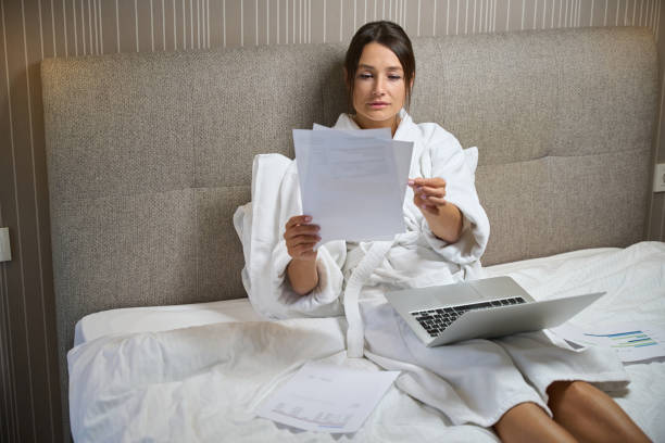 istock Businesswoman wearing bathrobe with laptop watching documents on bed 2118187873