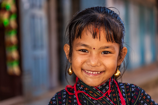 Portrait of young Nepali girl posing in an ancient town of Bhaktapur. She is wearing tradittional Newari dress. Bhaktapur is an ancient town in the Kathmandu Valley and is listed as a World Heritage Site by UNESCO for its rich culture, temples, and wood, metal and stone artwork.