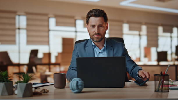 istock Positive boss putting cellphone working at modern agency. Manager looking laptop 2118216141