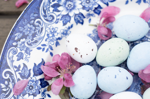 quail eggs painted blue on a vintage blue patterned plate decorated with pink petals, high quality photo
