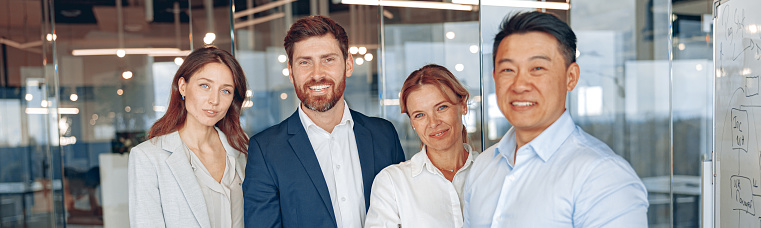 Happy diverse professional business team stand in office near each other looking at camera, smiling.