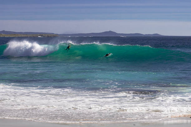 Cape Town, South Africa - May 31st, 2025: On a beach at Cape Town, a young surfer is watching the waves with his surfing board holding steady.  The morning sun didn't breakthrough the thick clouds, which makes the image more tranquil feeling.