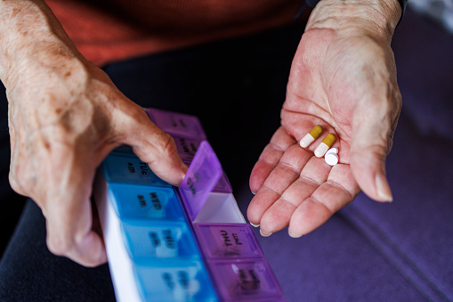 Close-up of unrecognizable senior woman hands with pill organizer, holding variety of pills. Aged female managing her prescribed medications for the week