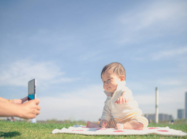 somebody taking picture of a baby sitting on grass by mobile phone