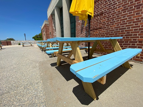 Row of picnic tables painted light blue with a yellow sun umbrella outside the Riis Beach Cooperative concession stand at historic Jacob Riis Park in the Rockaways, Queens, New York City