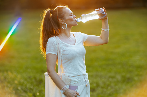 Summer time. relaxed young woman in white shirt with bottle of water in the meadow in the city park.