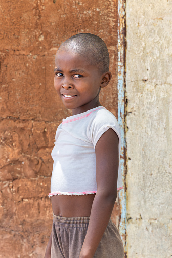 portrait of a single african villager girl standing outdoors in front of the house in a village,