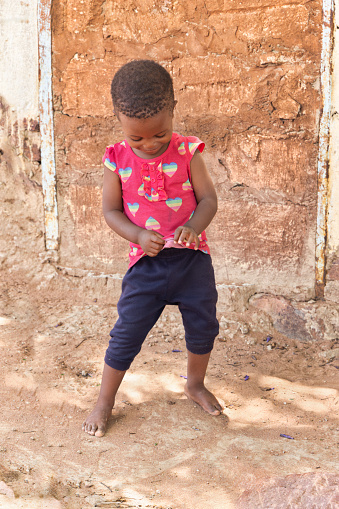 single african villager child playing outdoors in front of the house in a village,