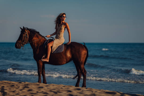 istock Lady is riding a horse on a beach while looking over her shoulder. 2118397640