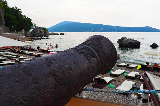 Herceg Novi Montenegro 08.09.22 A cannon, throwing device, type of artillery gun for firing at trajectory sea targets. Cast iron old cannon. Naval artillery. Coastal gun. People on the Adriatic beach.