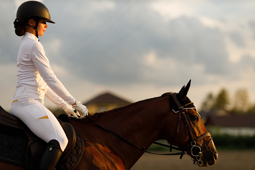 Woman rider jockey profile in helmet and white uniform preparing horse racing